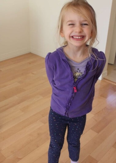 Young girl in purple shirt with hands behind back smiling