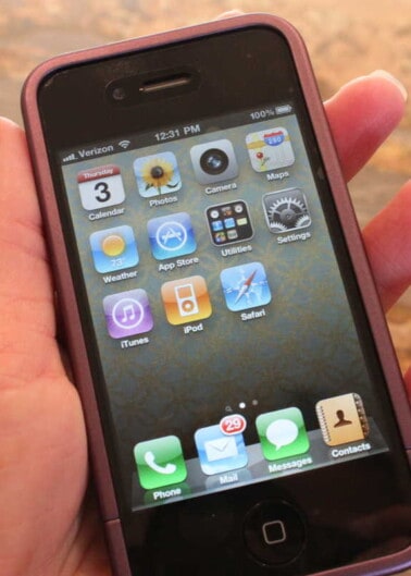 A hand holding an older model smartphone displaying the home screen with various app icons.