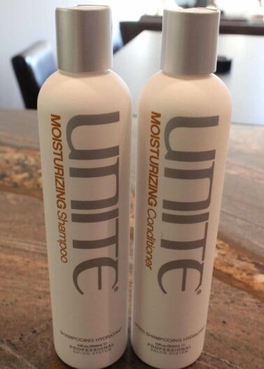 Two bottles of unite hair care products, one a moisturizing shampoo and the other a moisturizing conditioner, placed side by side on a wooden surface.