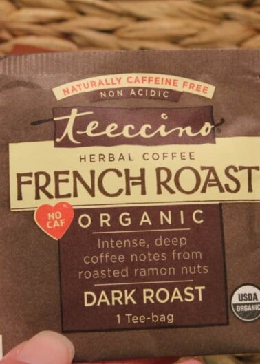 A hand holding a packet of teeccino herbal coffee french roast, a naturally caffeine-free and non-acidic alternative to coffee.