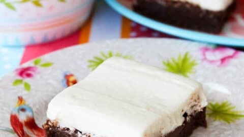 A piece of frosted brownie on a colorful floral napkin with more brownies and a patterned bowl in the background.