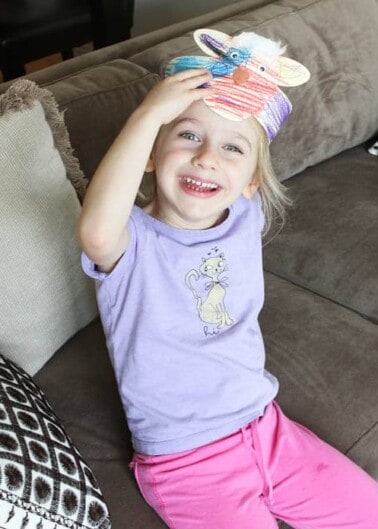 A young girl smiling with a colorful stuffed toy on her head.