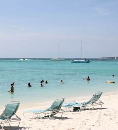 Beachgoers enjoying the water with lounge chairs on the shore and boats in the distance.