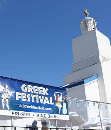 A banner promoting a greek festival in front of a white church with a blue sky in the background.