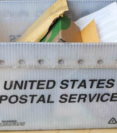 A usps mail tote filled with various envelopes and packages.