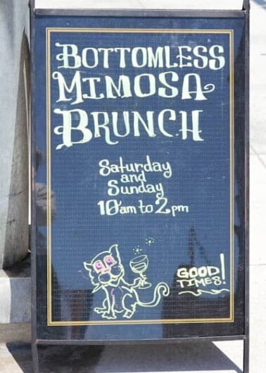 Sidewalk sign advertising bottomless mimosa brunch available saturday and sunday from 10 am to 2 pm, featuring playful cat illustrations and the phrase "good times!.