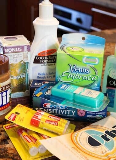 An assortment of personal care and household items on a counter, including toothpaste, shaving razors, lotion, deodorant, gum, and peanut butter.