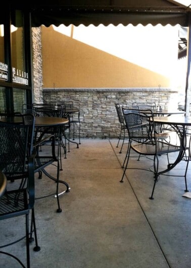 An empty outdoor seating area with metal chairs and tables under an awning.