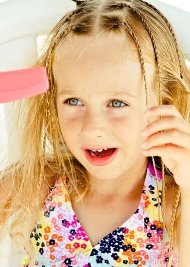 Young girl combing her hair with a pink comb.