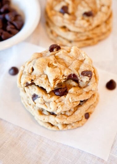 Stack of chocolate chip cookies on a table with loose chocolate chips in the background.