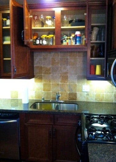 A kitchen corner featuring dark wood cabinets, a stainless steel sink, and a gas stove with beige tile backsplash.