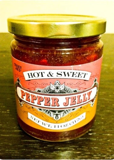 A jar of trader joe's hot & sweet pepper jelly on a wooden surface.