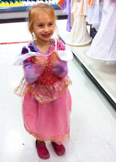 Young girl wearing a princess costume and smiling inside a store.