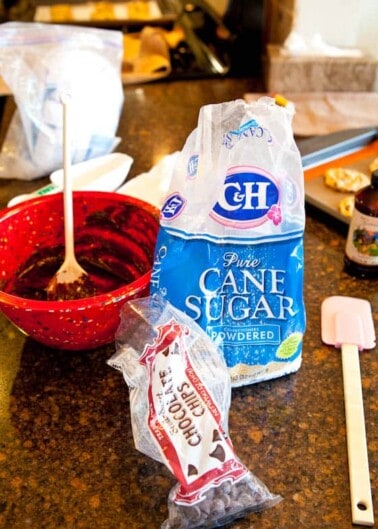 Kitchen countertop with an open bag of powdered sugar, a red bowl with a mixture, and cooking utensils.