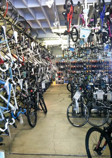 Rows of assorted bicycles displayed in a bike shop with accessories on the wall.