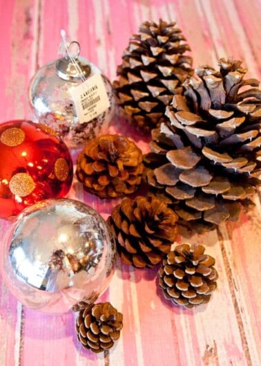 Christmas ornaments and pine cones arranged on a pink wooden surface.