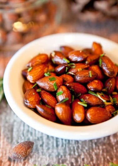 A bowl of roasted almonds garnished with herbs.