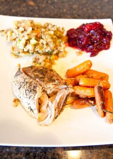 Roasted chicken with carrots, stuffing, and cranberry sauce on a white plate.