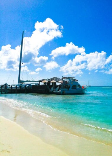 A sailboat moored near a pier on a sunny beach with clear blue skies.