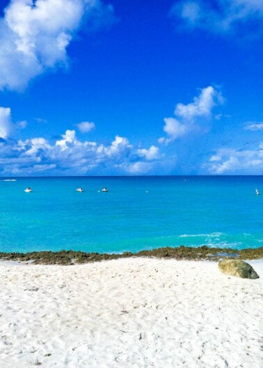 Tropical beach with clear blue sky, turquoise water, and people on paddleboards in the distance.