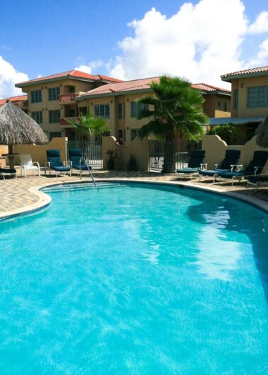 Swimming pool at a tropical resort with sun loungers and palm trees under a clear blue sky.