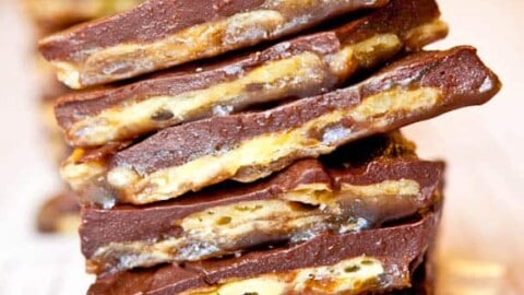 A stack of chocolate-covered toffee bars on a wooden surface.