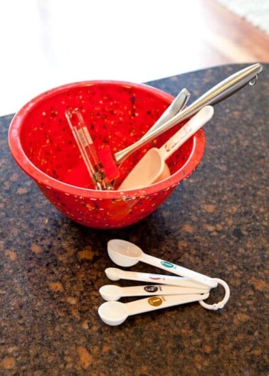 A red colander with kitchen utensils on a countertop.