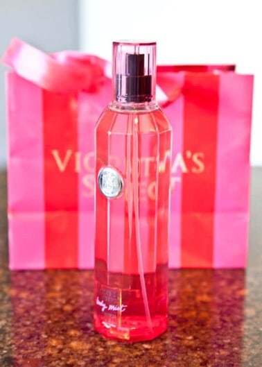 A bottle of victoria's secret body mist with a branded shopping bag in the background.