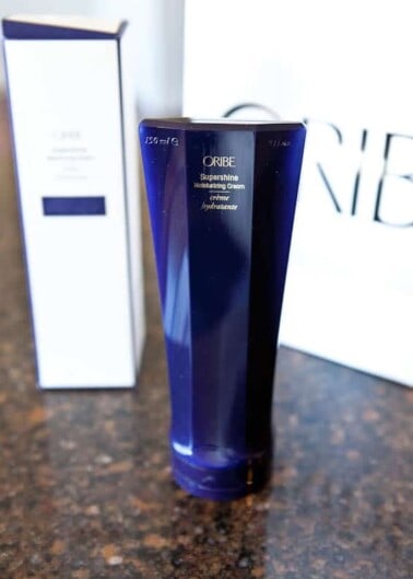 A tube of oribe supershine moisturizing cream placed on a countertop with its packaging box in the background.