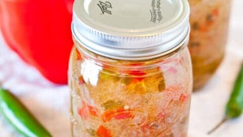 Three jars of homemade salsa with a red bell pepper and a jalapeño pepper in the background.