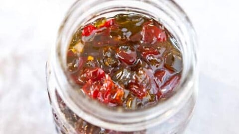 Open jar of jam with a spoon nearby on a white surface.