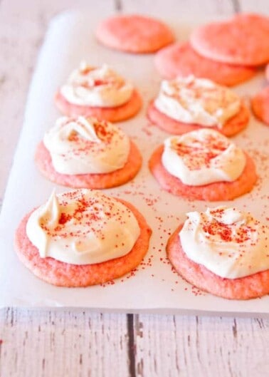 Pink cookies topped with cream cheese frosting and a sprinkle of red sugar.