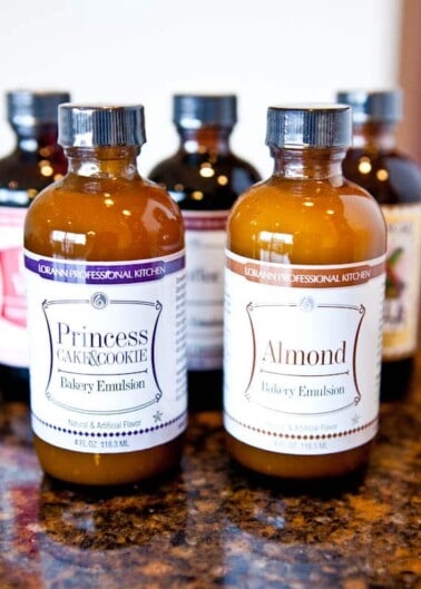 Bottles of bakery emulsion flavors, including princess cake & cookie and almond, on a kitchen countertop.