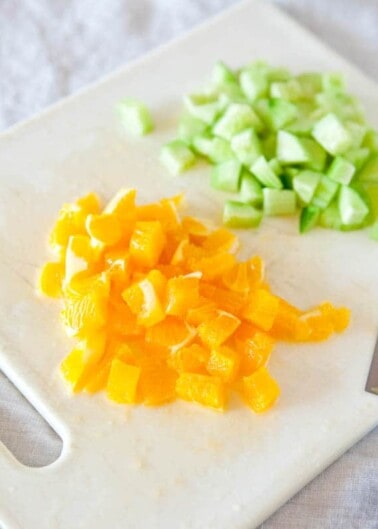 Chopped yellow bell pepper and cucumber on a white cutting board.