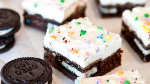 Chocolate brownies topped with cream and colorful sprinkles, accompanied by sandwich cookies.