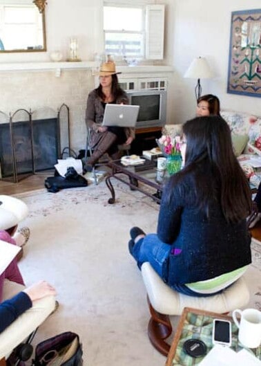 A group of individuals participating in an indoor meeting or workshop, sitting in a circle in a cozy living room setting.