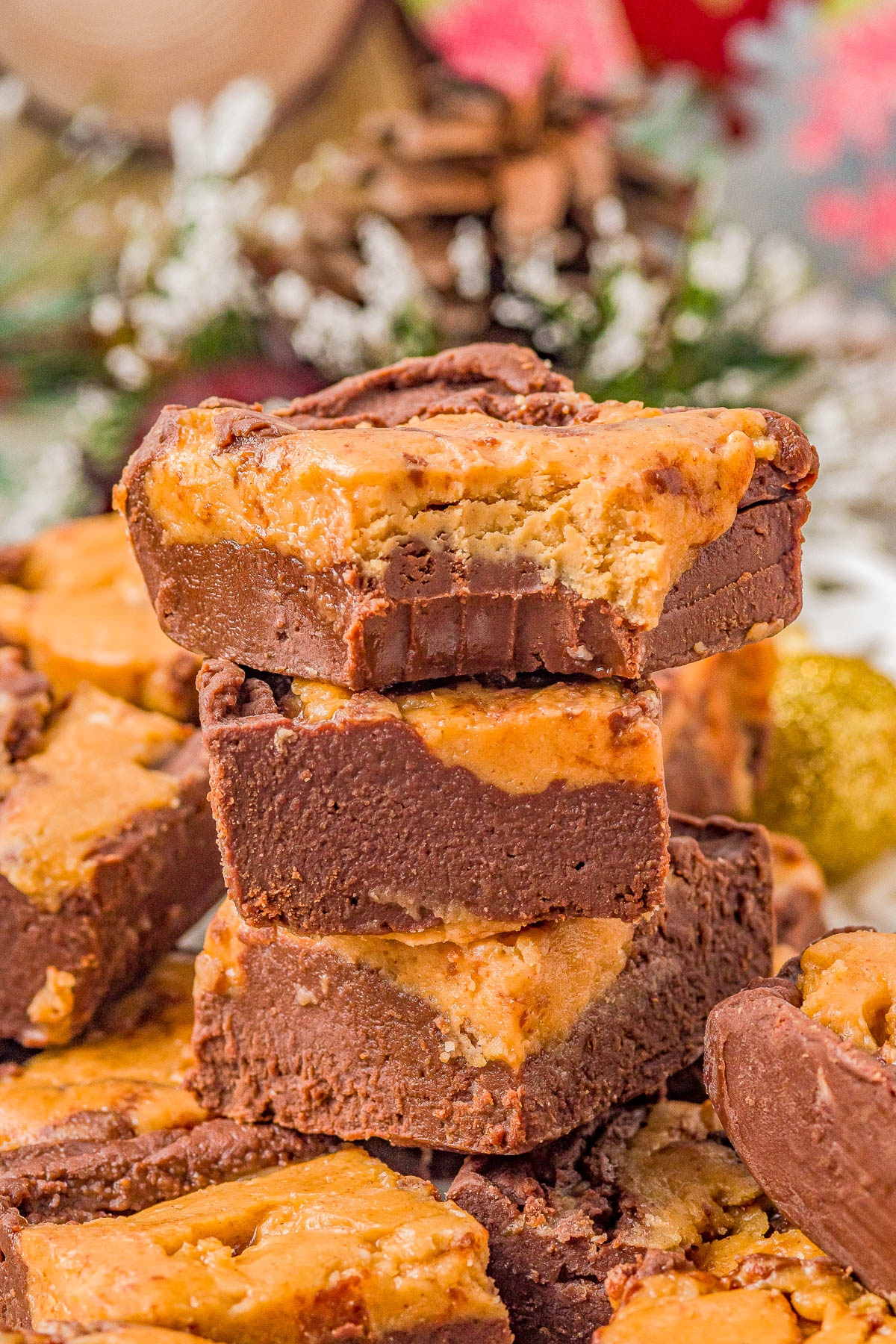 A stack of chocolate peanut butter brownies with a bite taken out of the top piece, surrounded by more brownies and festive background decor.