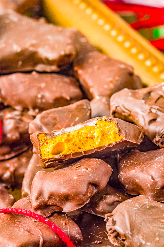 Pile of chocolate-covered honeycomb toffee pieces, one with a bite showing the golden interior.