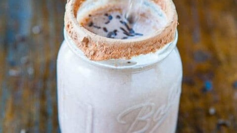 Mason jar filled with a chocolate milkshake and a metal straw, with a cocoa powder rim, on a wooden surface.