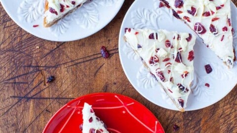 Slices of white chocolate bark with cranberries and nuts served on various colored plates.