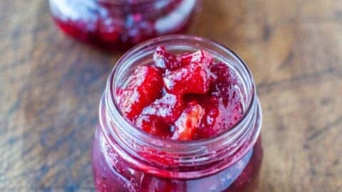 Two jars of homemade cranberry sauce on a wooden surface.