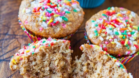 Freshly baked muffins with colorful sprinkles on a wooden surface.