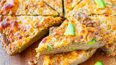 A freshly baked quiche with avocado slices on a wooden cutting board.