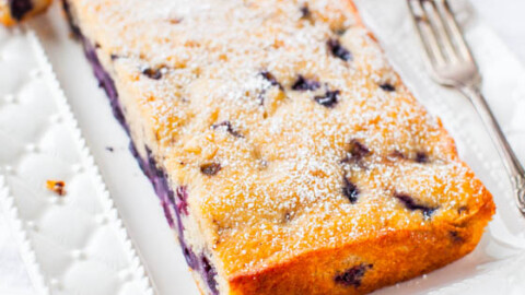 A blueberry loaf cake dusted with powdered sugar on a decorative plate with two forks.