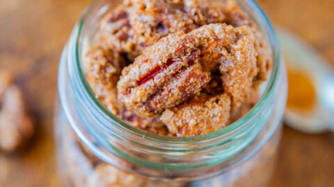 Candied pecans in a glass jar with more nuts and a honey dipper in the background.