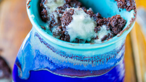 A blue ceramic mug filled with mint chocolate chip ice cream on a wooden surface.