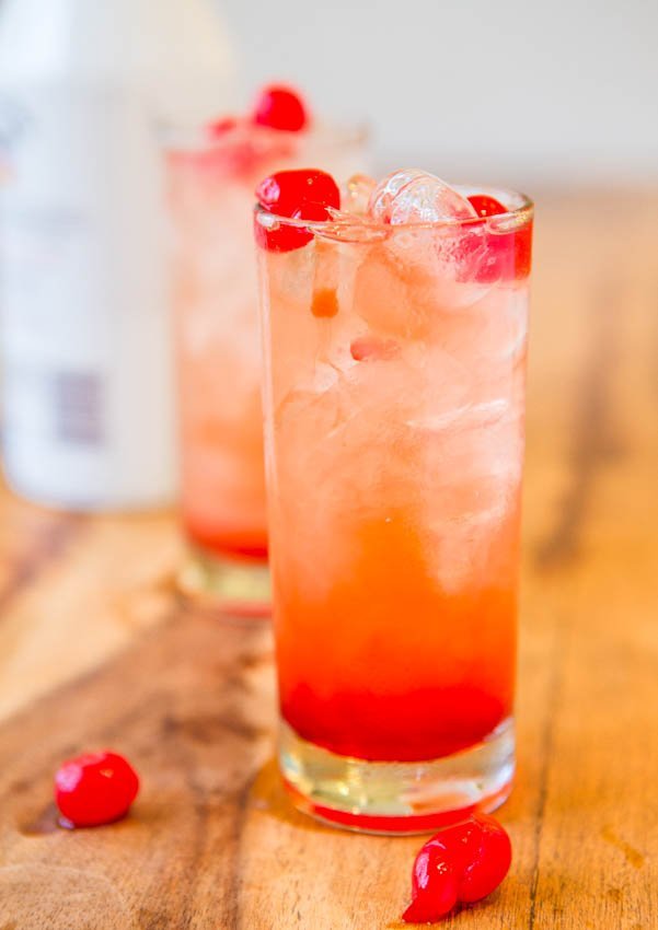 A refreshing glass of iced red cocktail garnished with cherries on a wooden surface.