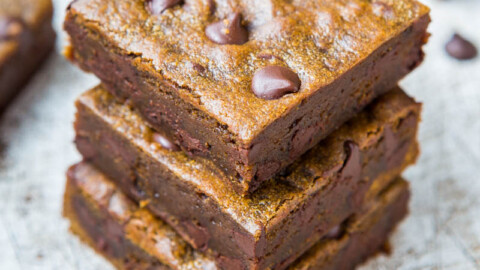 A stack of three homemade chocolate chip brownies on a white surface.