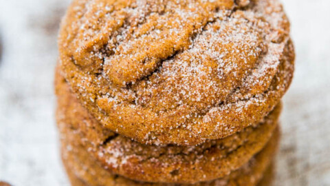 A stack of sugar-coated ginger cookies on a wooden surface with a spoonful of syrup nearby.