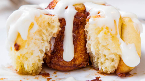 A cinnamon roll with icing on a white plate.